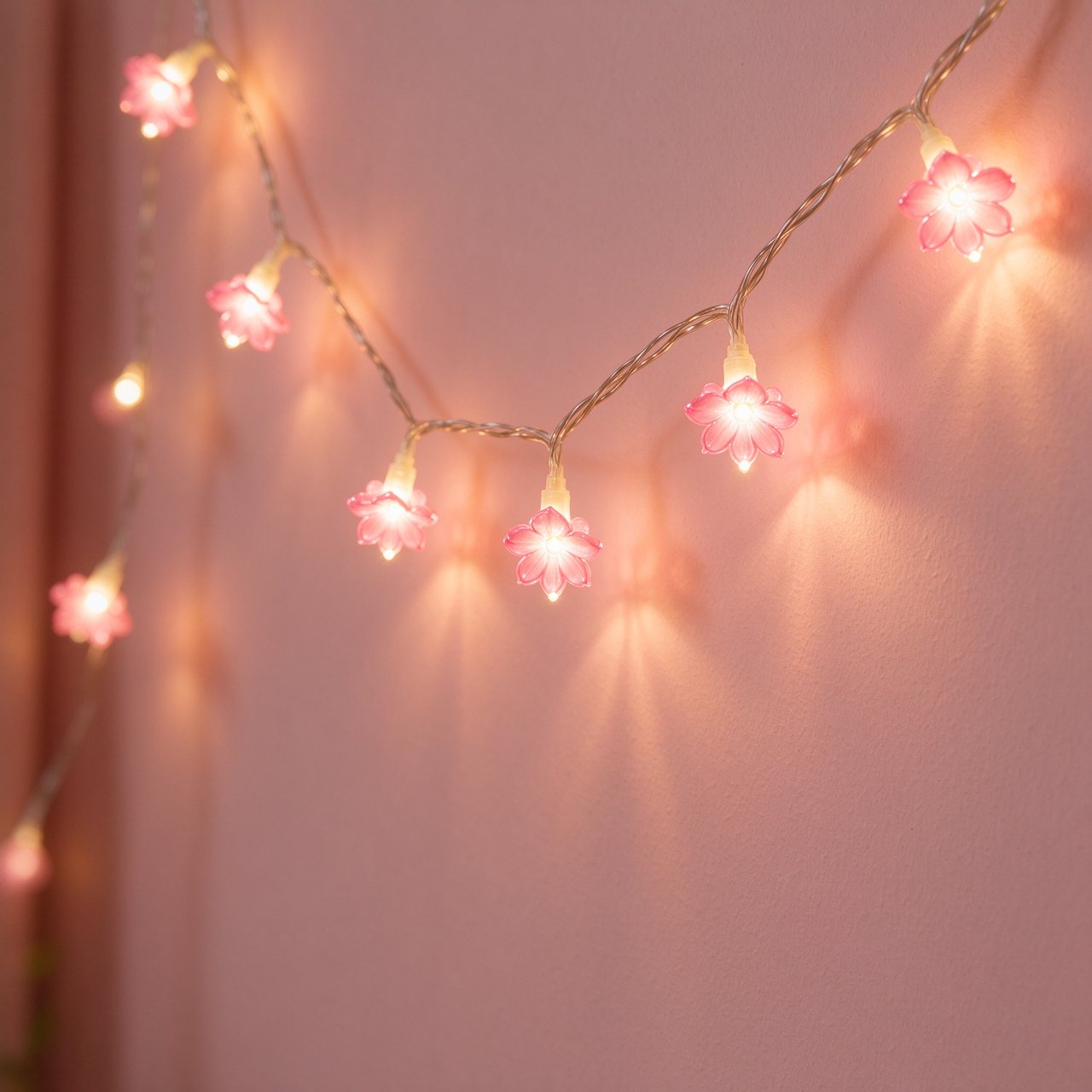 Warm fairy lights with pink flower-shaped bulbs on a blush wall
